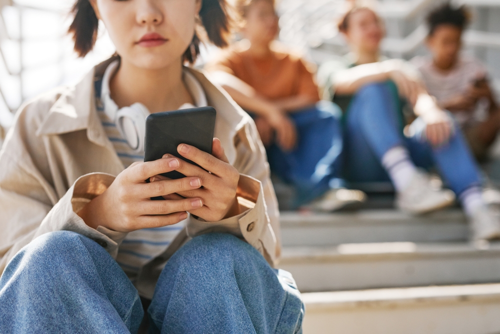 Closeup Of Teenage Girl Holding Smartphone Outdoors While Sitting On Stairs