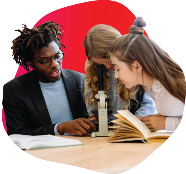 Educator speaking to two students who are looking through a microscope and reading