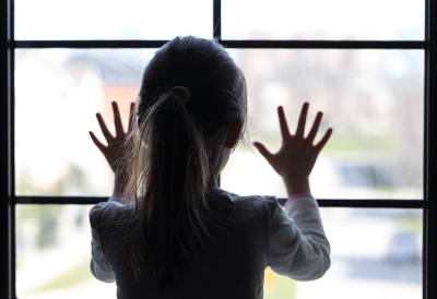 Silhouette of a young child looking out the window with hands on the glass