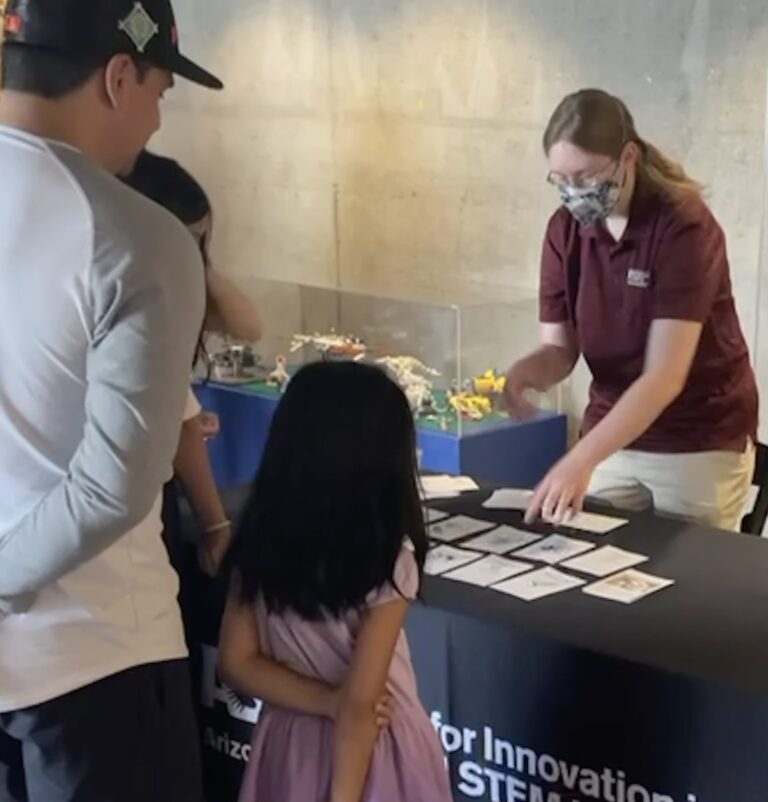 Photo of Claire standing at a table showing onlookers various cards