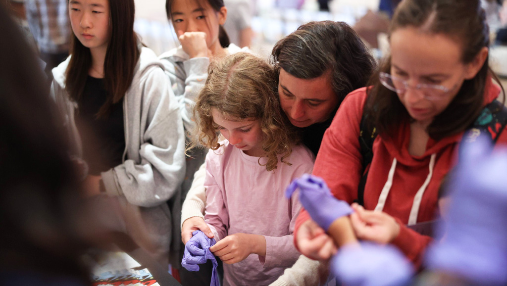 Photo of parent helping their child put on lab gloves at science conference